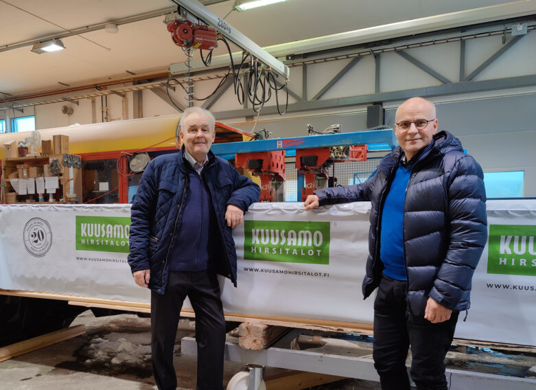 Jouko Virranniemi ja Arto Orjasniemi seisovat tuotantohallissa pakatun hirsipaketin vieressä.