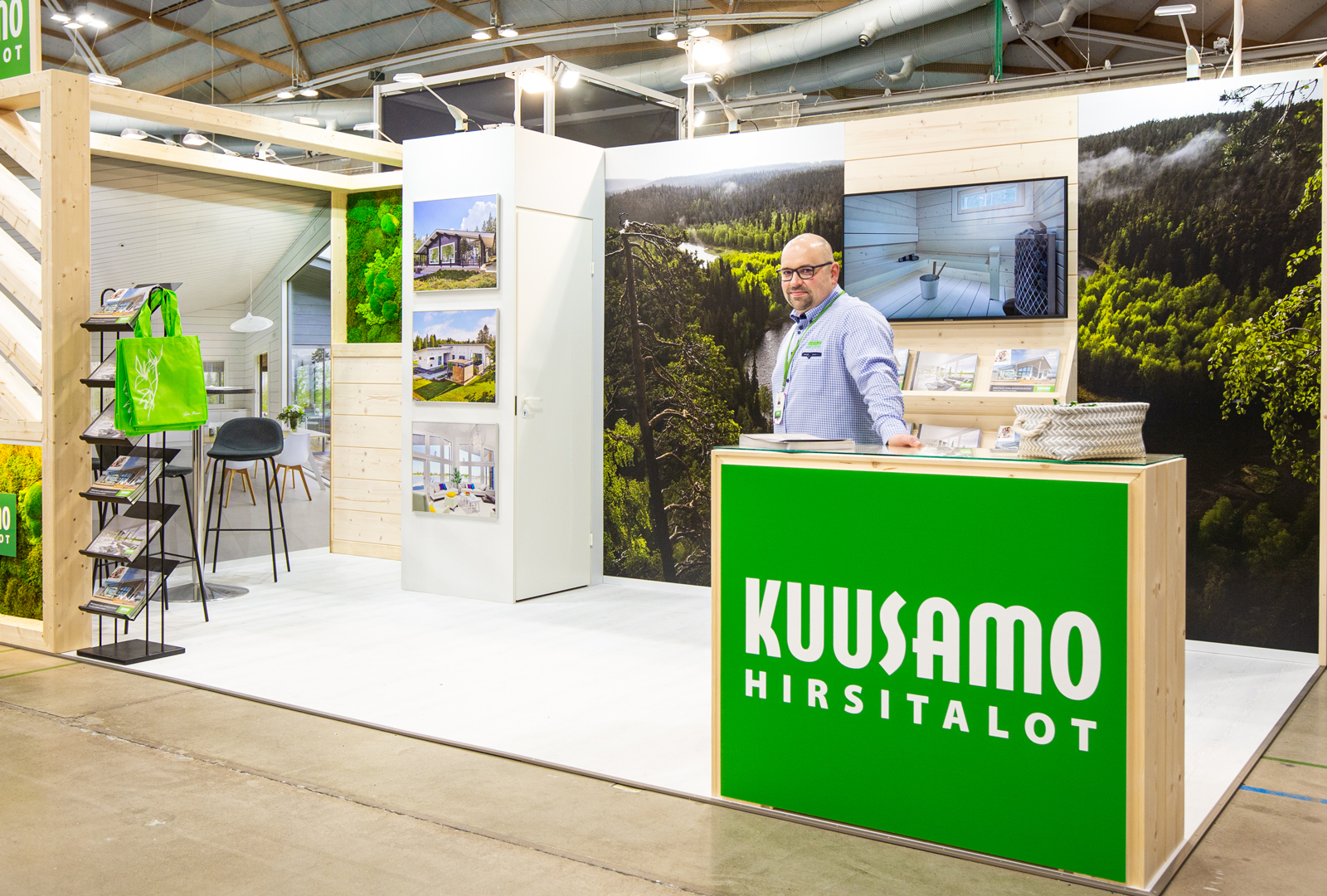 Kuusamo-myyjä seisoo Kuusamo Hirsitalojen messuosastolla.