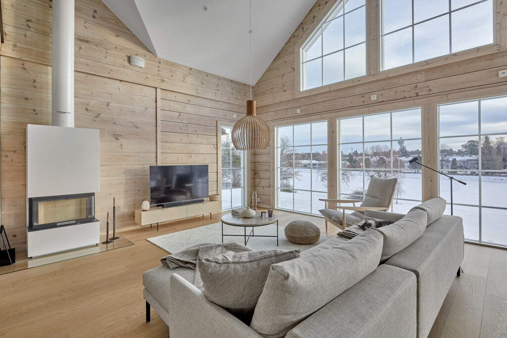 The Suvela living area from the log house collection. The wood-toned interior complements the atmosphere of the view through the large windows.