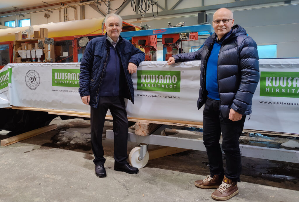 Vd Arto Orjasniemi och styrelseordförande Jouko Virranniemi står bredvid ett timmerpaket i Kuusamo Timmerhusets produktionshall.
