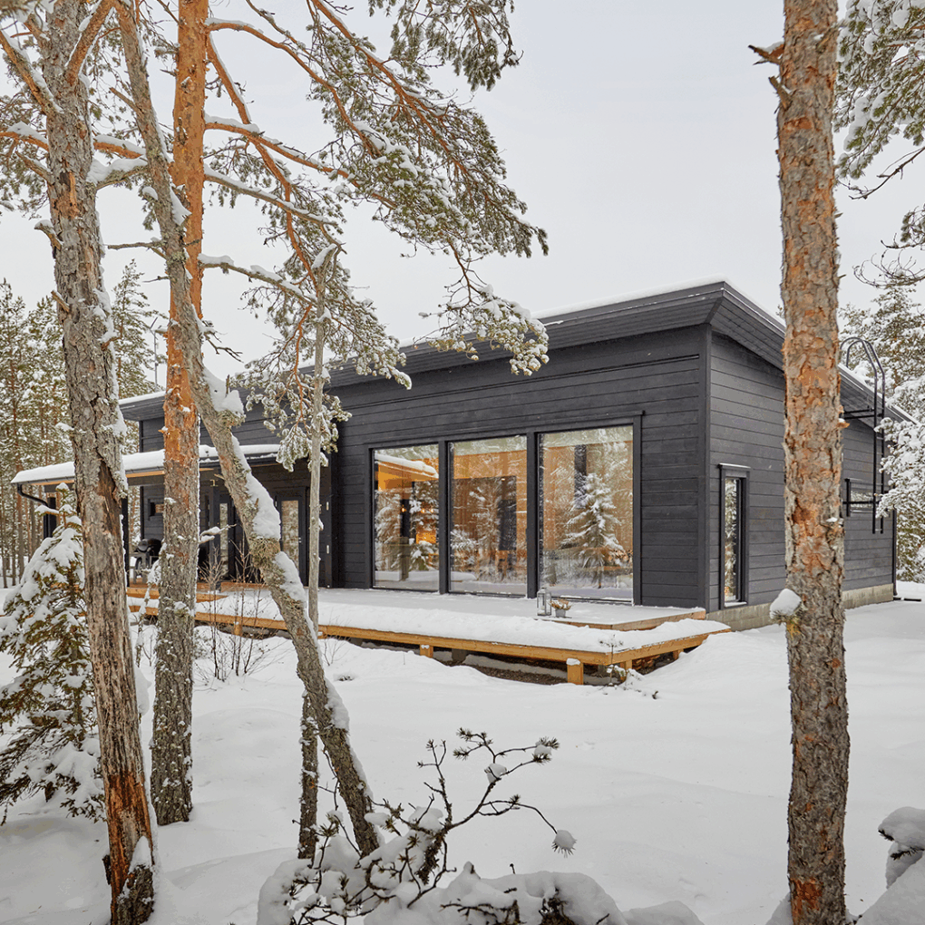 The black, modern log house blends in perfectly with the pine forest.