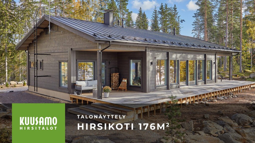 Harjakattoinen harmaaksi maalattu hirsikoti mäntymetsäisellä tontilla.
