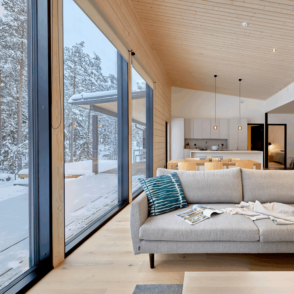 The living room of the log house features large windows opening out onto the snow-covered forest.
