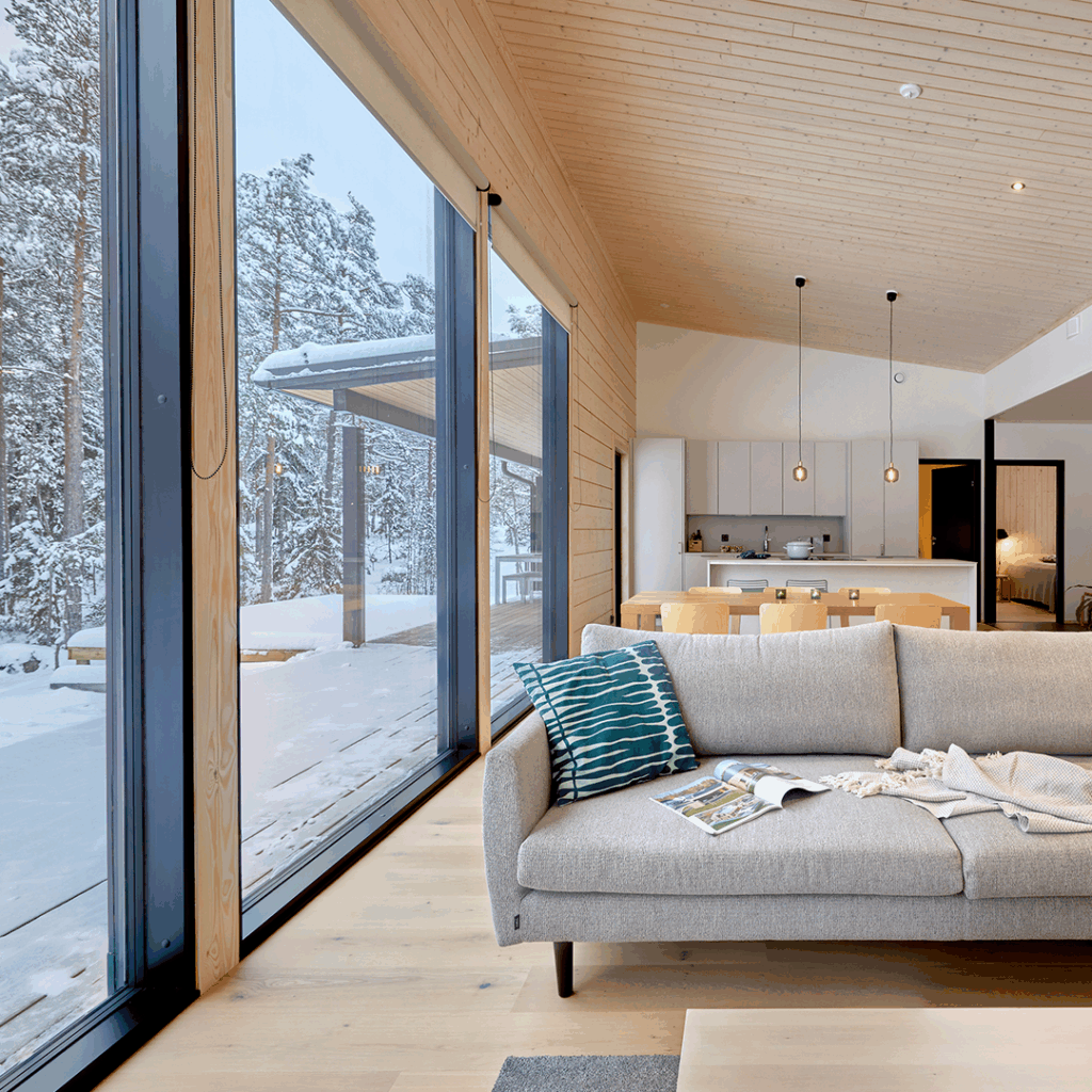 Vardagsrummet i timmerhuset har stora fönster som vetter mot den snötäckta skogen.