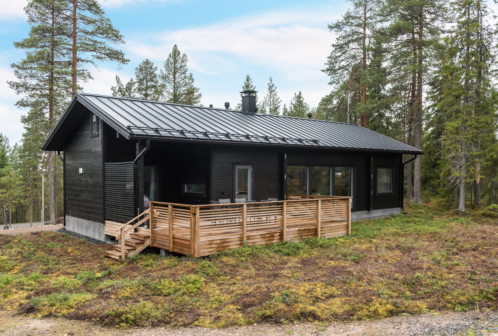 Tummaksi väritetty harjakattoinen hirsikoti Oulanka. Takapihalla on tilava terassi.