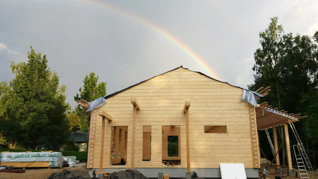 Bild på ett timmerhus under uppförande. Regnbågen verkar sluta vid huset, det är en skatt.