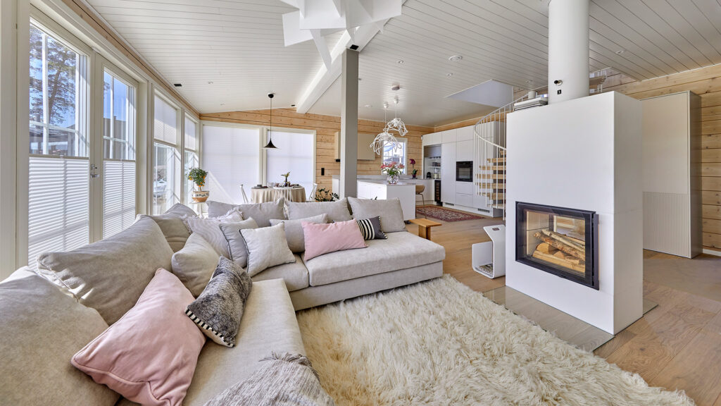 The living room of the log house, featuring a relaxing corner sofa and a tunnel fireplace separating the hallway from the living room.