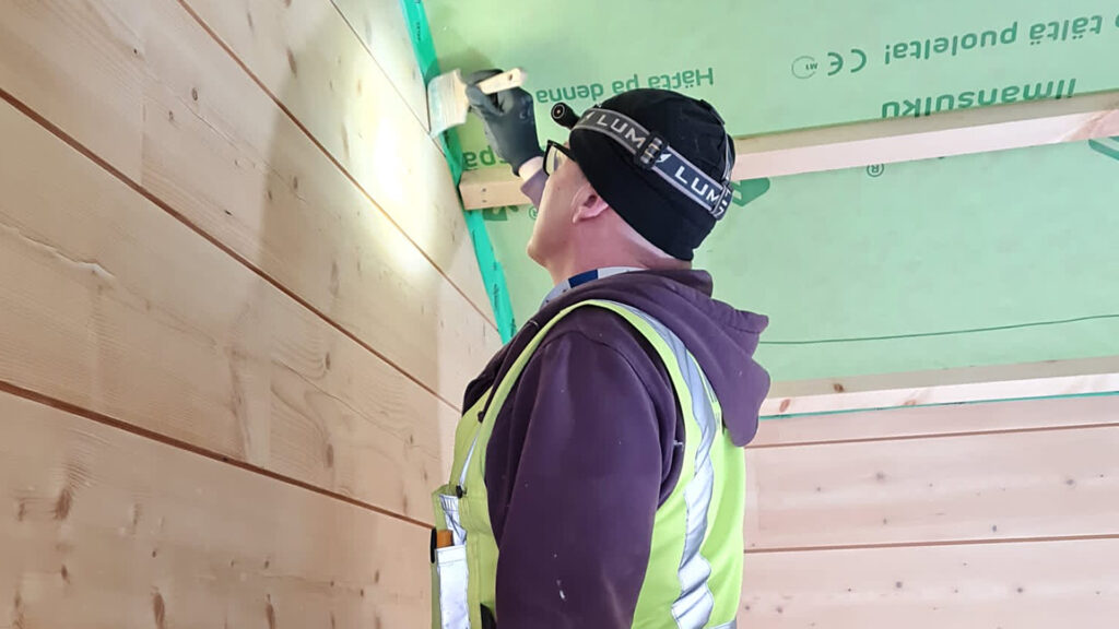 A resident of the house working on the log walls. The ceiling has yet to be fitted, but the battens for the ceiling panels are already in place.