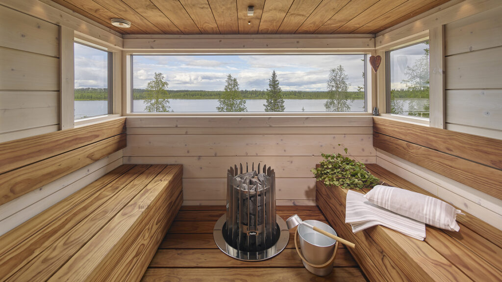 Saunasta aukeaa panoraama-tyyliset ikkunat järvimaisemiin. Saunan seinät ovat vaaleat, mutta lauteet ja katto on tummanruskeat.