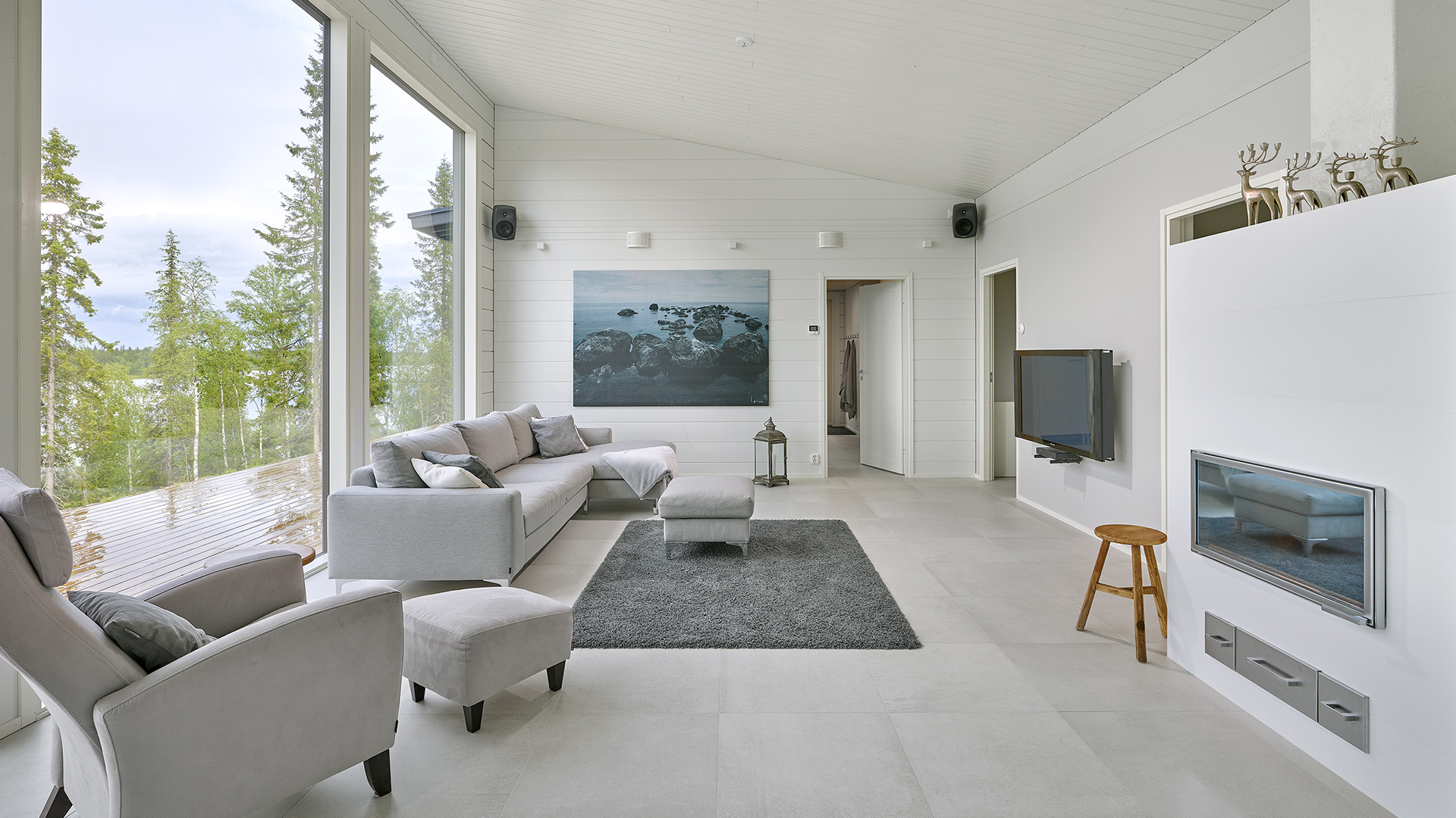 The living room of a house with a pitched roof, where the roof rises up to the front wall of the building. The white walls and ceiling emphasise the sense of space in this already bright room.