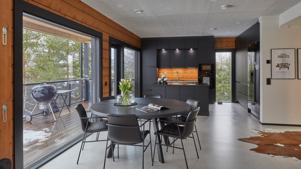 The kitchen units are black. The orange-brown treated logs complement them perfectly. The floor is laid with large tiles.