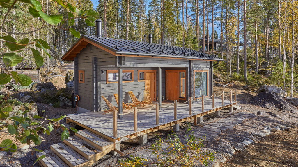 Saunamökki harjakatolla toteutettuna. Kompakti saunamökki on harmaaksi ja oranssiksi käsitelty.