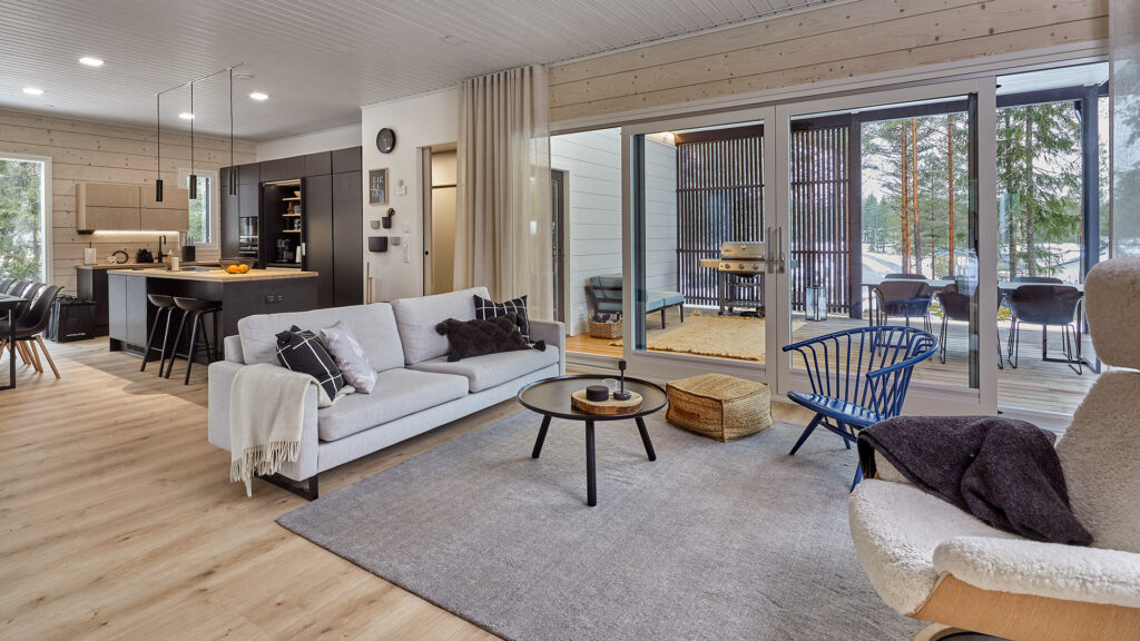 The living room of the log house, with large windows opening onto the terrace and the surrounding countryside. The blue Artek Crinolette armchair stands out beautifully against the otherwise calm interior.