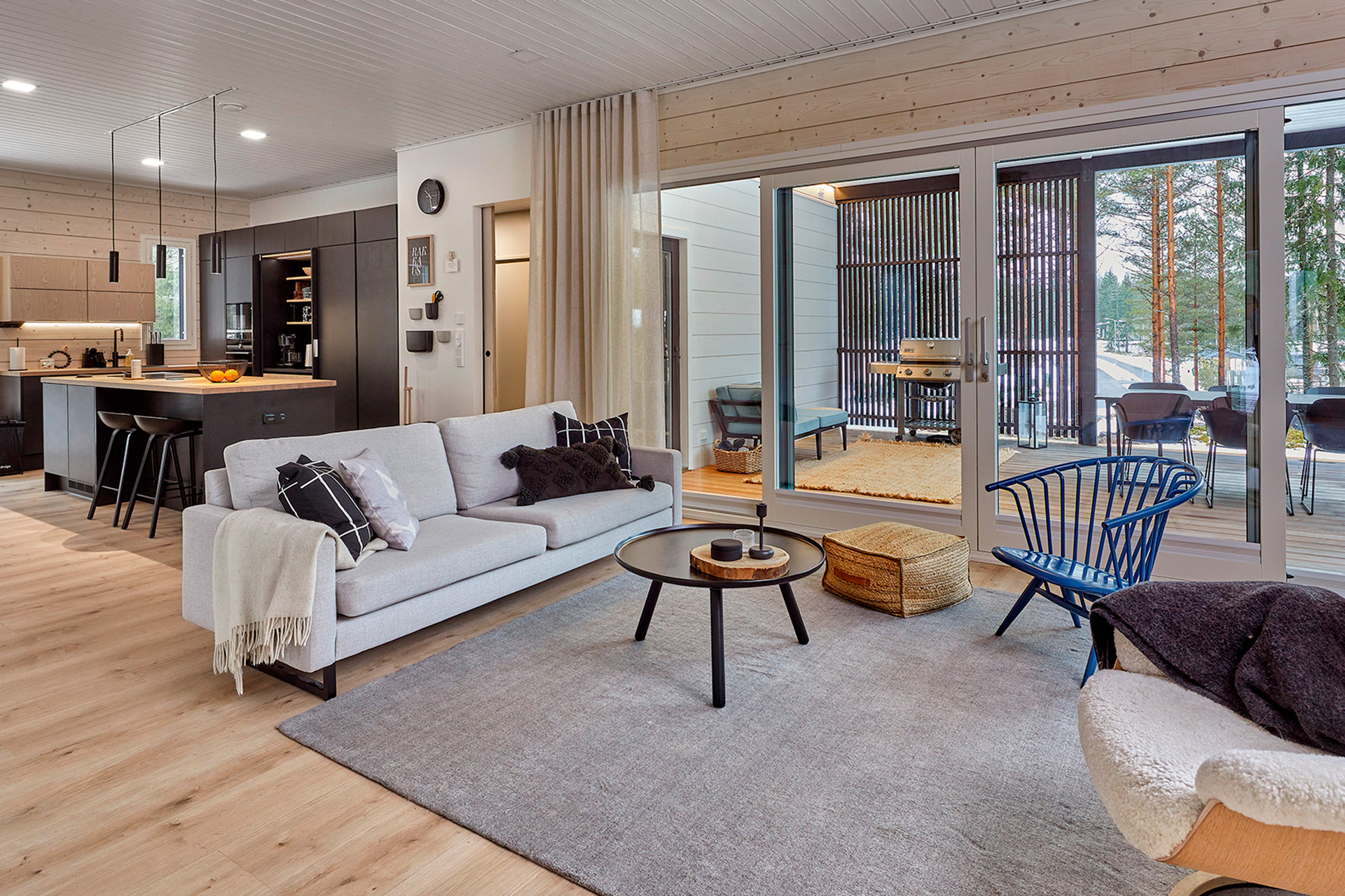 The living room of the log house, with large windows opening onto the terrace and the surrounding countryside. The blue Artek Crinolette armchair stands out beautifully against the otherwise calm interior.