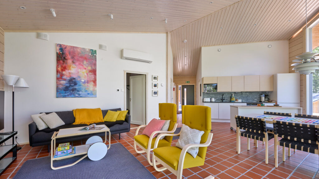 A living room decorated in bright colours. The yellow armchairs and cushions, as well as the colourful painting on the wall, are the living room’s standout features.