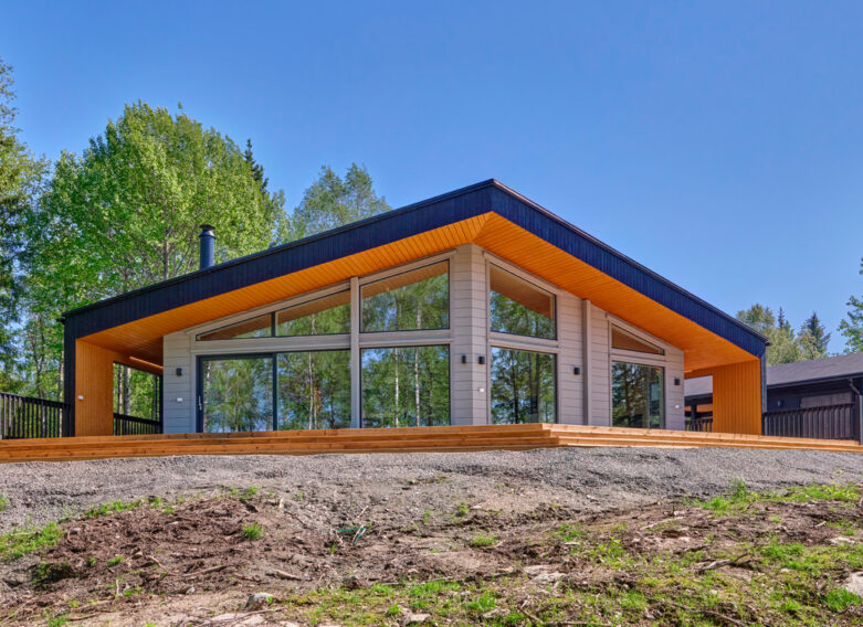 A modern log villa, finished in black, orange and grey. The front wall of the building features large windows.