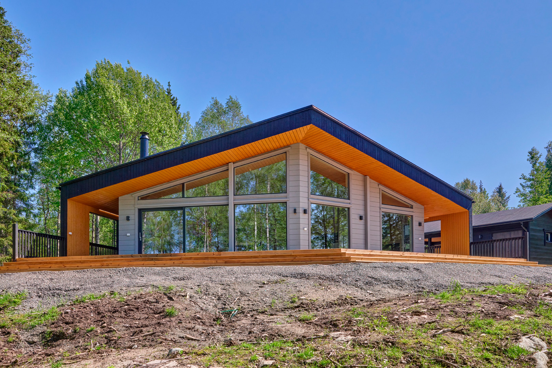 A modern log villa, finished in black, orange and grey. The front wall of the building features large windows.