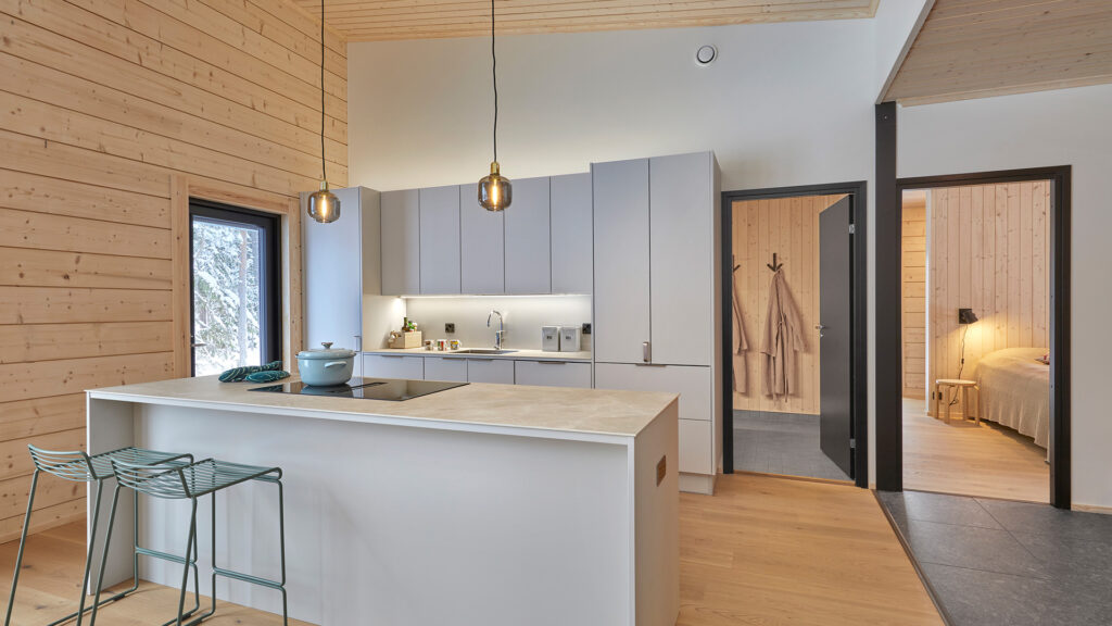 The kitchen of a log house, with grey fitted units. The logs are nicely visible on one wall of the kitchen.