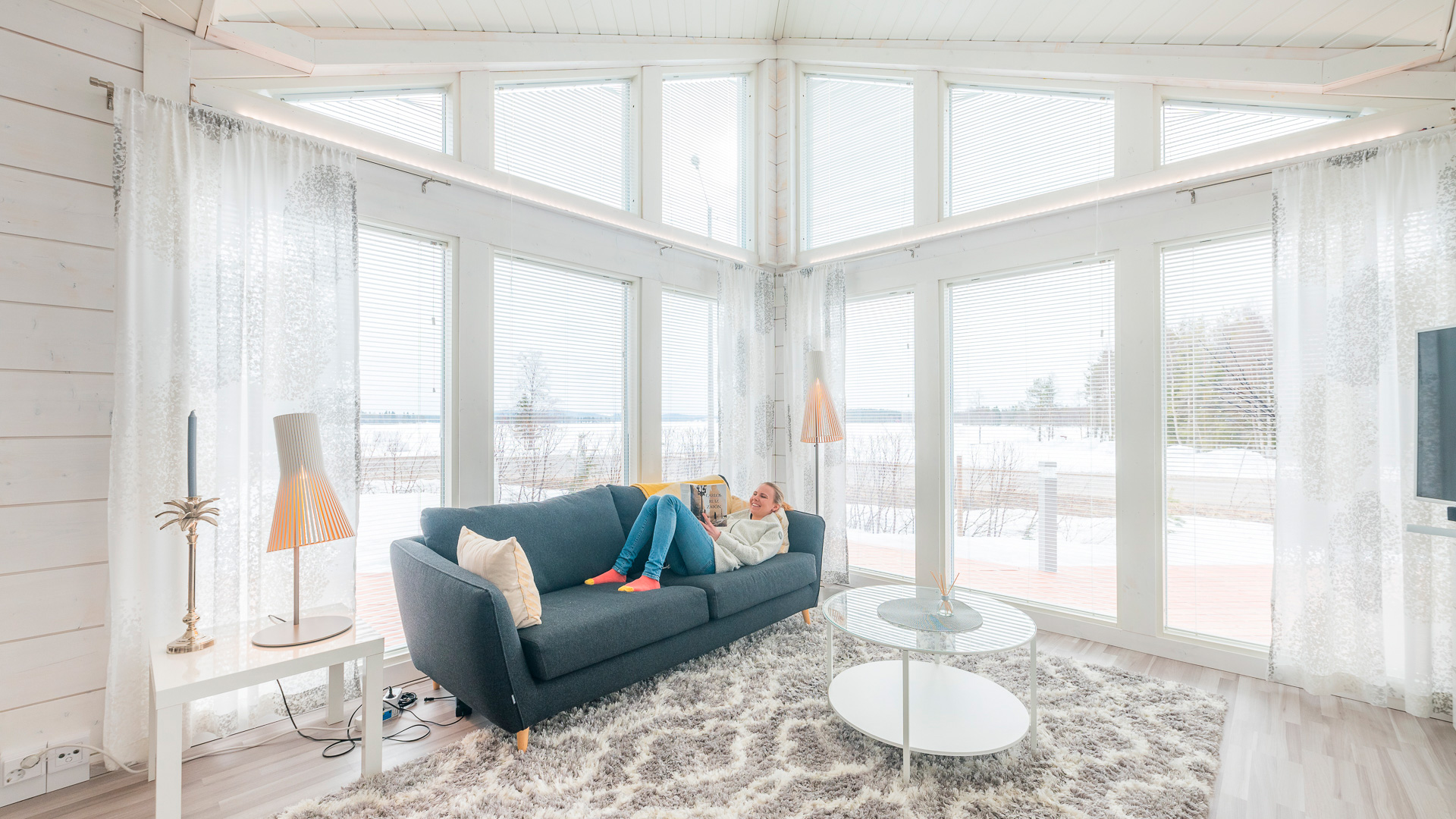 The light-coloured living room of a log house, where Susanna Saapunki is reading a magazine on the sofa.