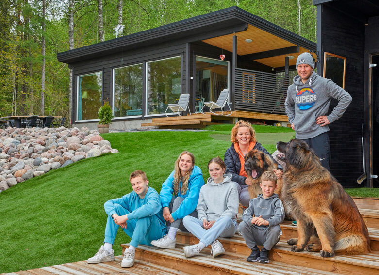 Familjen Helenius framför sin timmerstuga. Familjen består av föräldrarna, fyra barn och två hundar.
