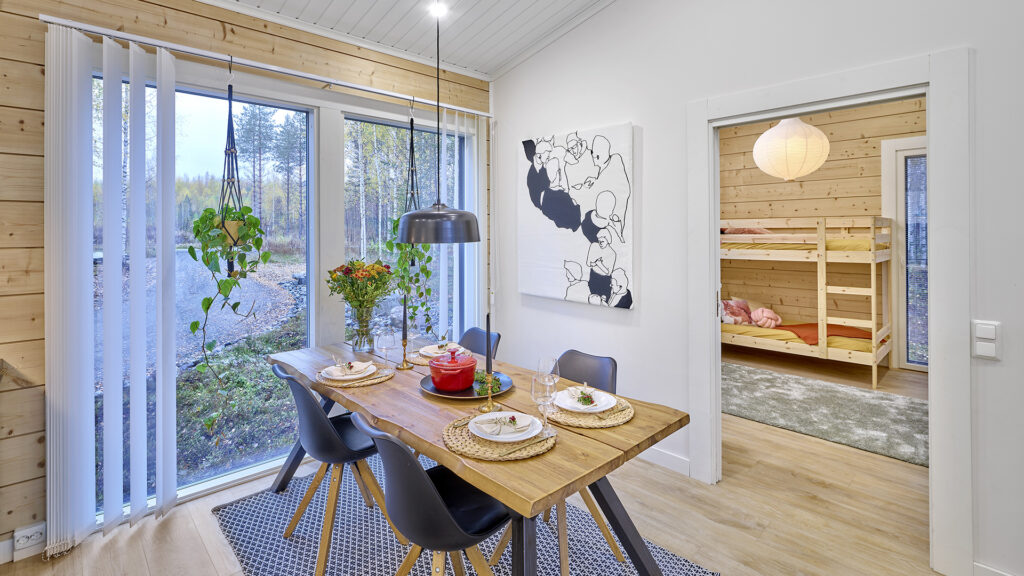Ruokailutila, jonka yhteydessä on lattiasta lähtevät ikkunat. Ruokapöytä on massiivipuusta valmistettu.