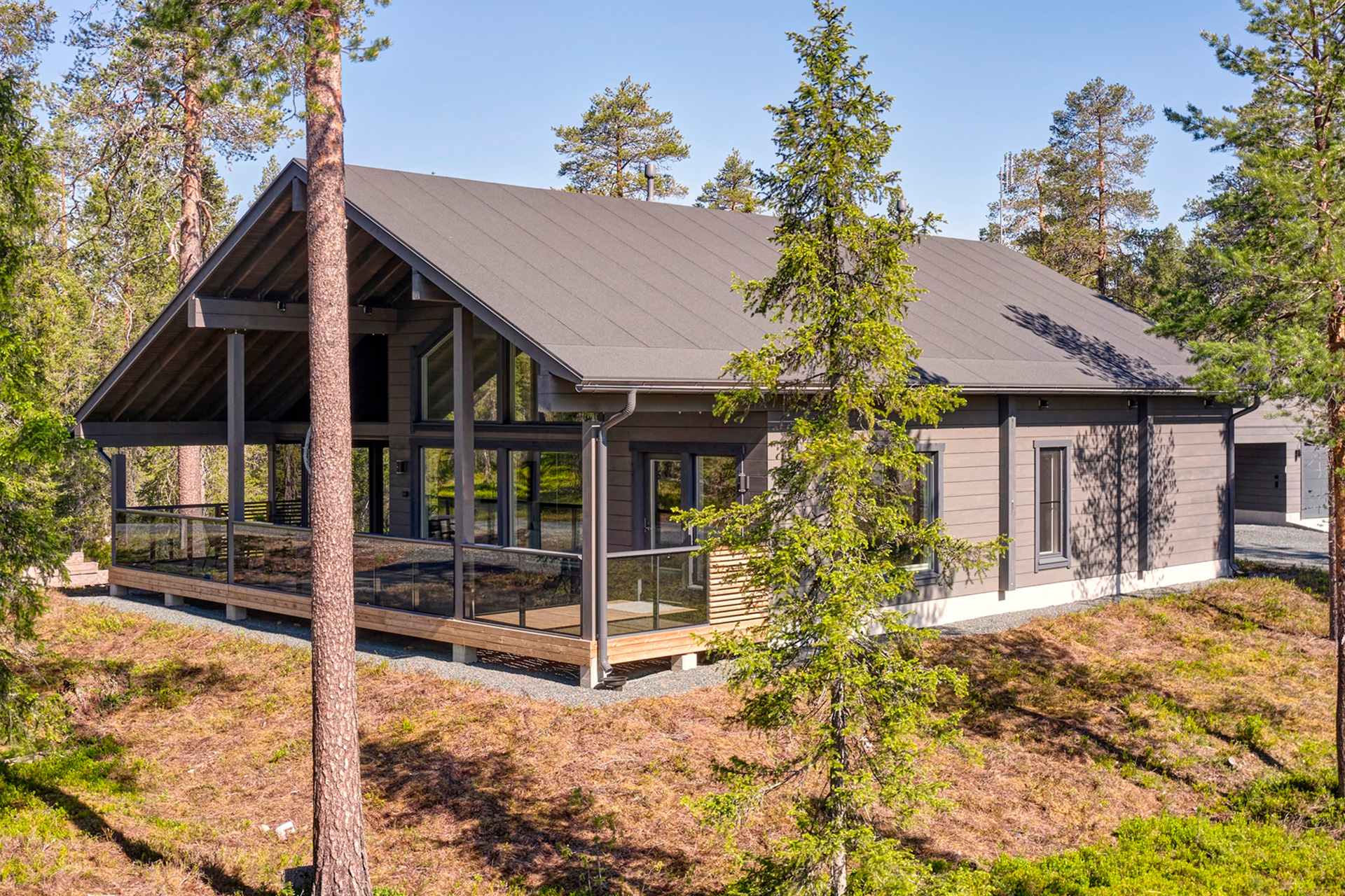 Harjakattoinen hirsitalo huopakatolla toteutettuna. Harjakatto jatkuu rakennuksen etupuolelle koko terassin matkalle.
