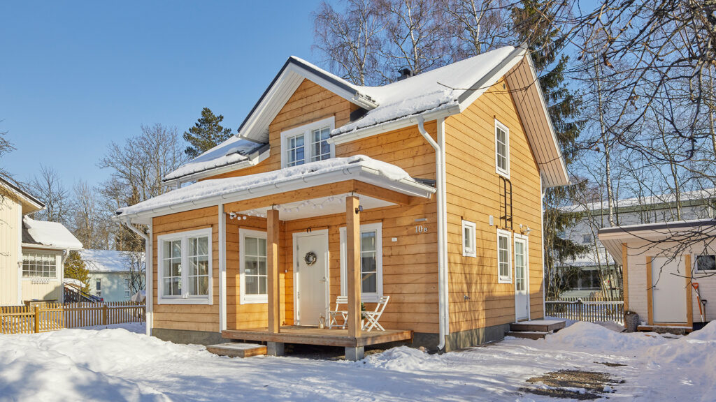 A small log house with a pitched roof. The log walls have been treated with a translucent finish and the details are finished in white.