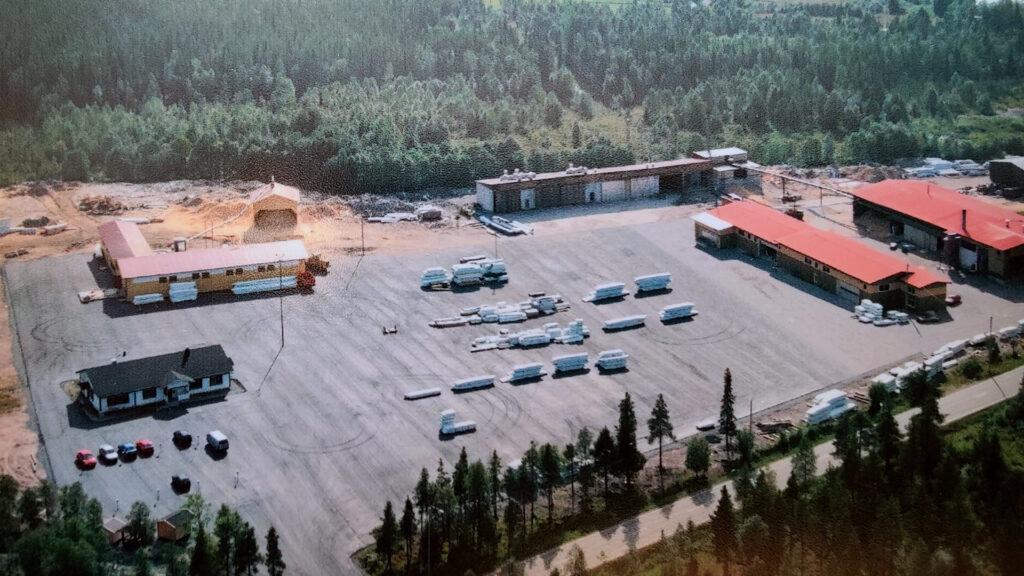 Kuva Kuusamo Hirsitalojen tehdasalueesta 2000-luvun alusta. Pihapiiristä löytyy toimisto. tuotantohalleja, sekä hirsi- ja puutavarapakettijonoja.