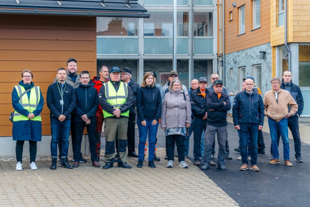 Some of the staff at Kuusamo Log Houses standing in the courtyard of a log-built apartment block.