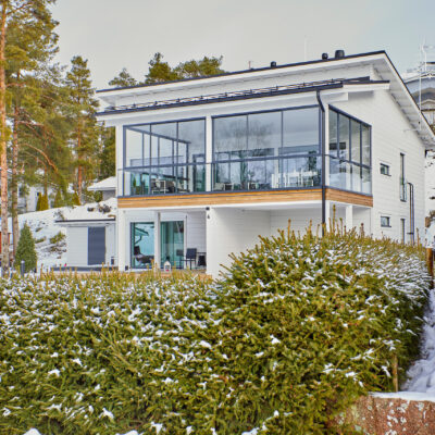 Modernin, valkoisen hirsitalon tonttia ympäröi pensasaita.