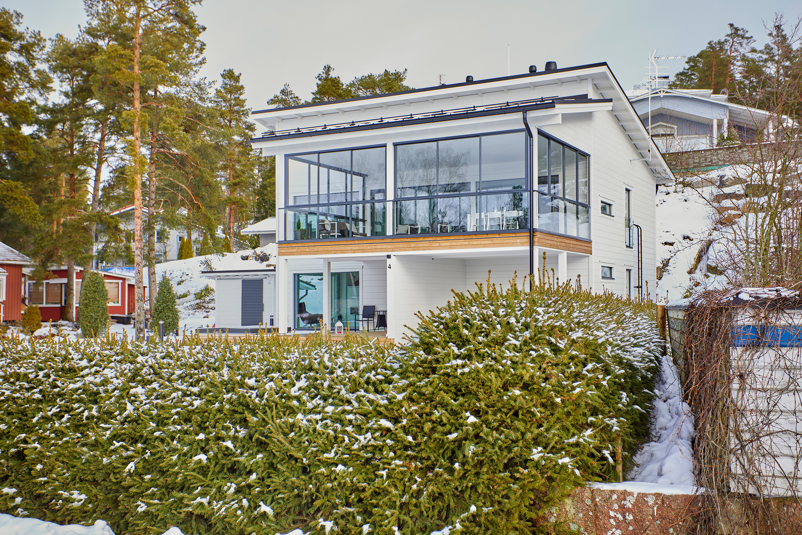 Modernin, valkoisen hirsitalon tonttia ympäröi pensasaita.
